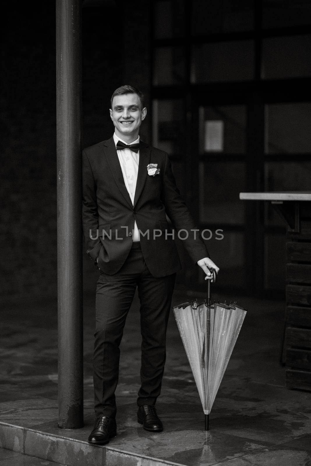 portrait of a young guy groom in a black suit on a rainy day