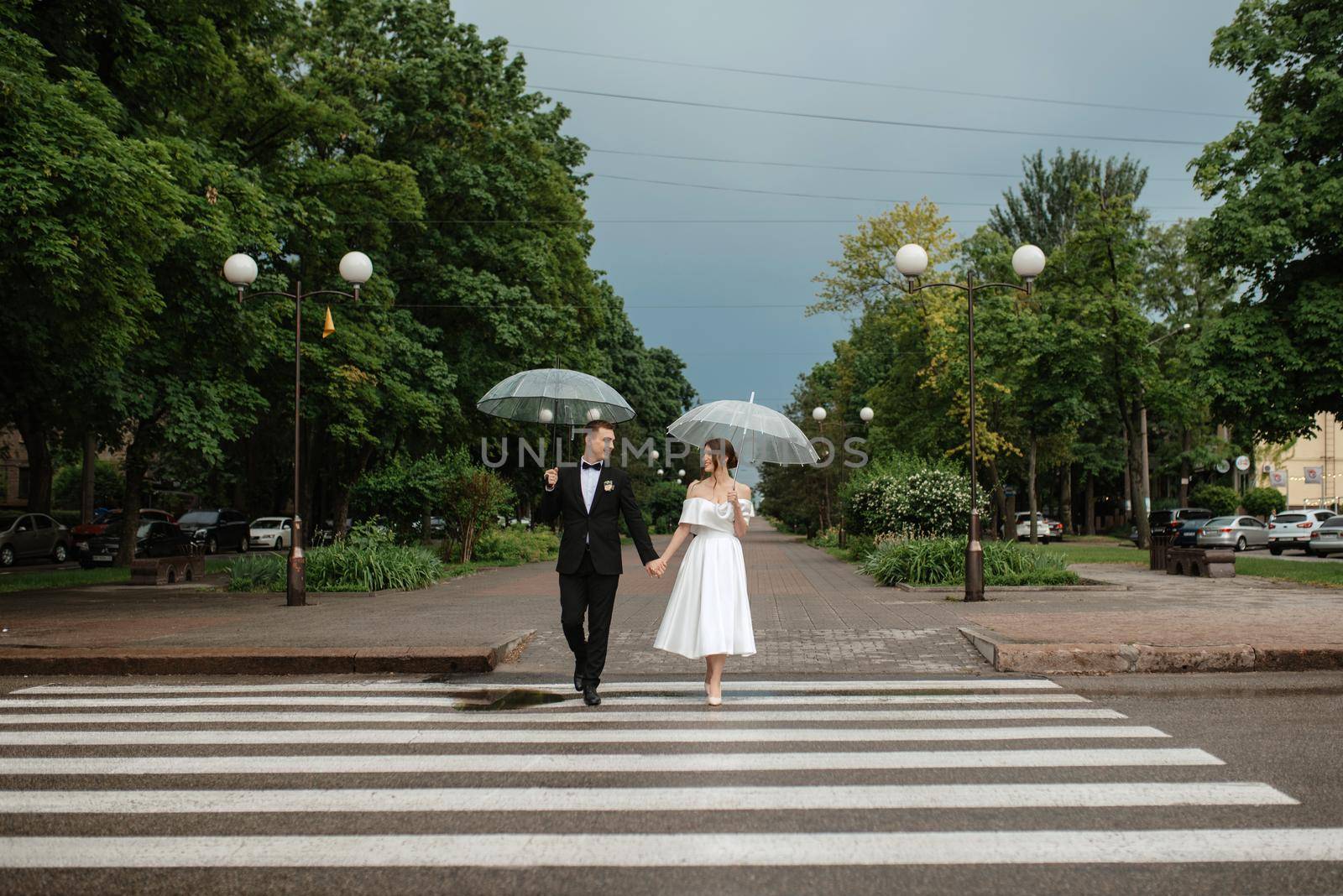 young couple bride and groom in a white short dress walking in the rain