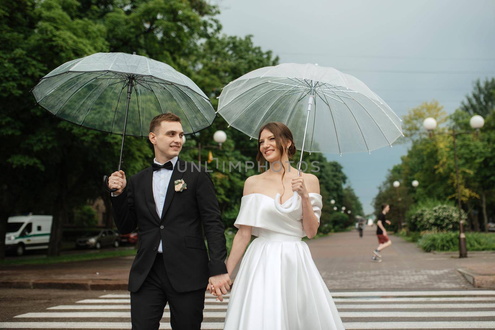 young couple bride and groom in a white short dress walking in the rain