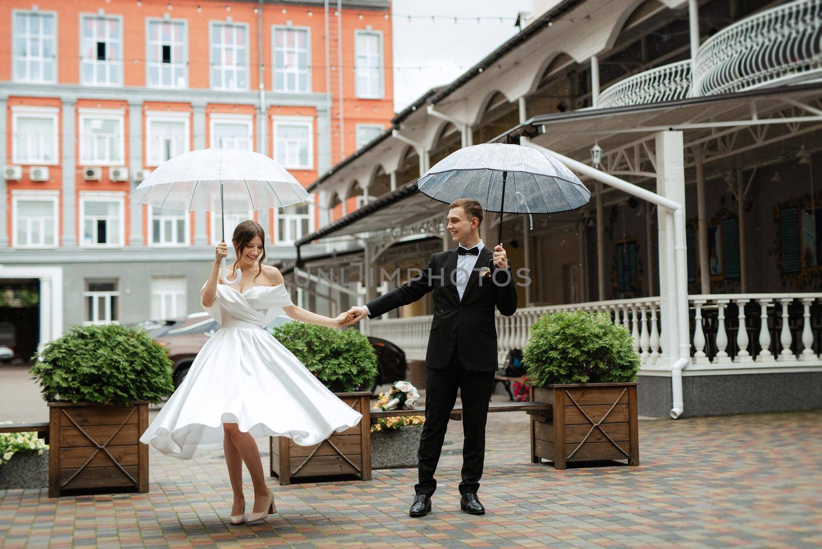 young couple bride and groom in a white short dress walking in the rain