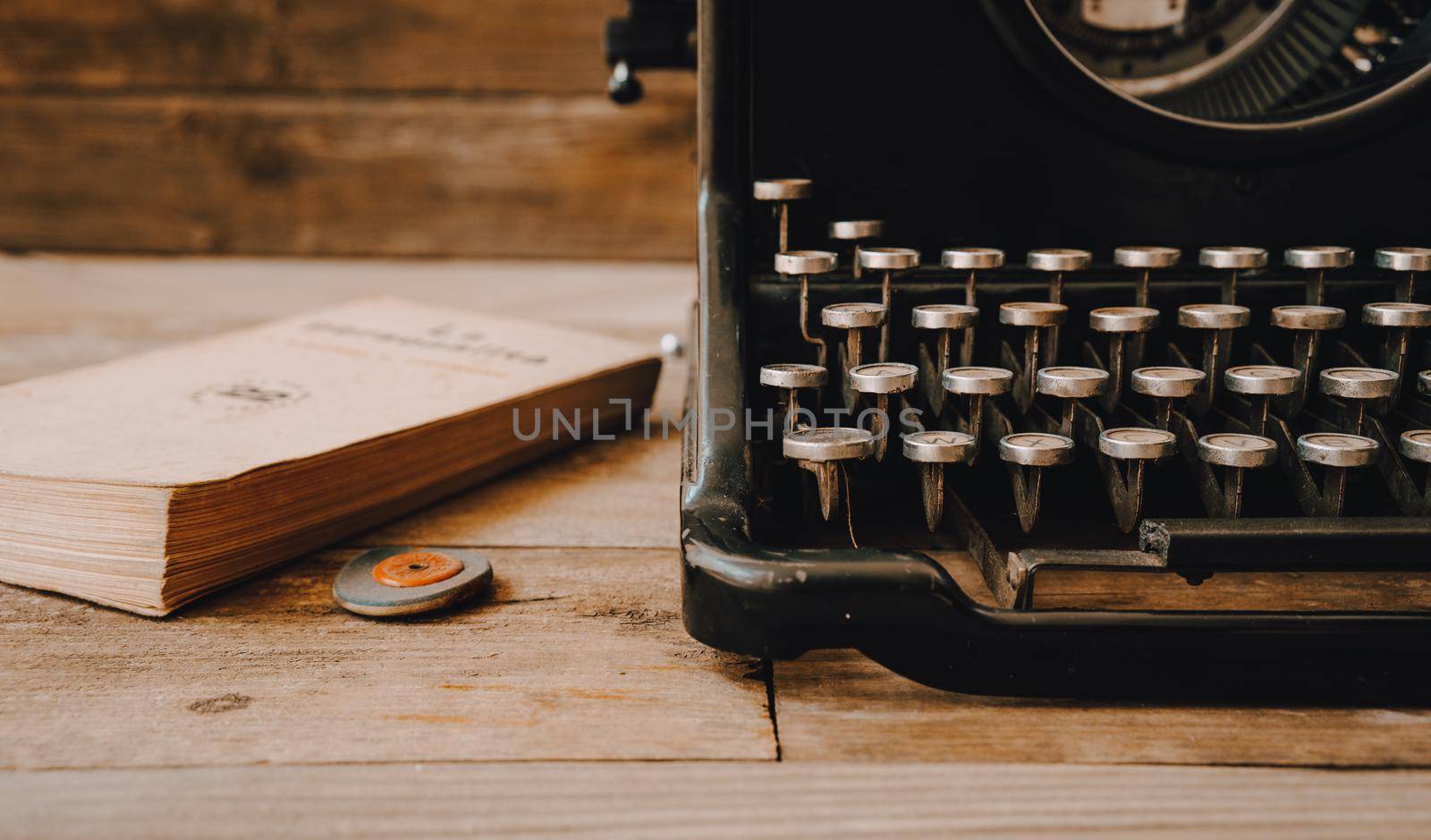 A black vintage typewriter with a rubber and an old book on wooden background.