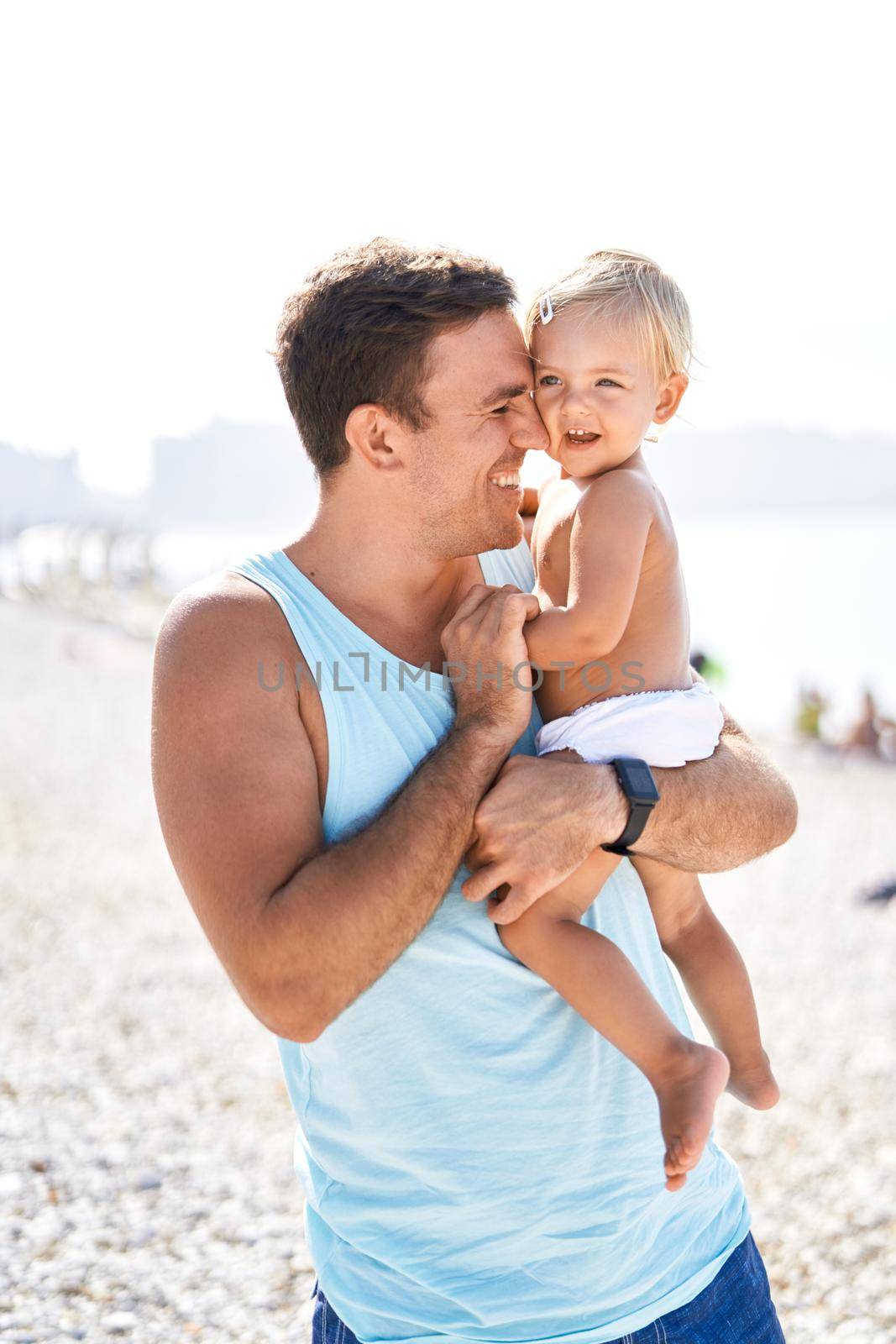 Laughing dad with little daughter in his arms on the beach. High quality photo