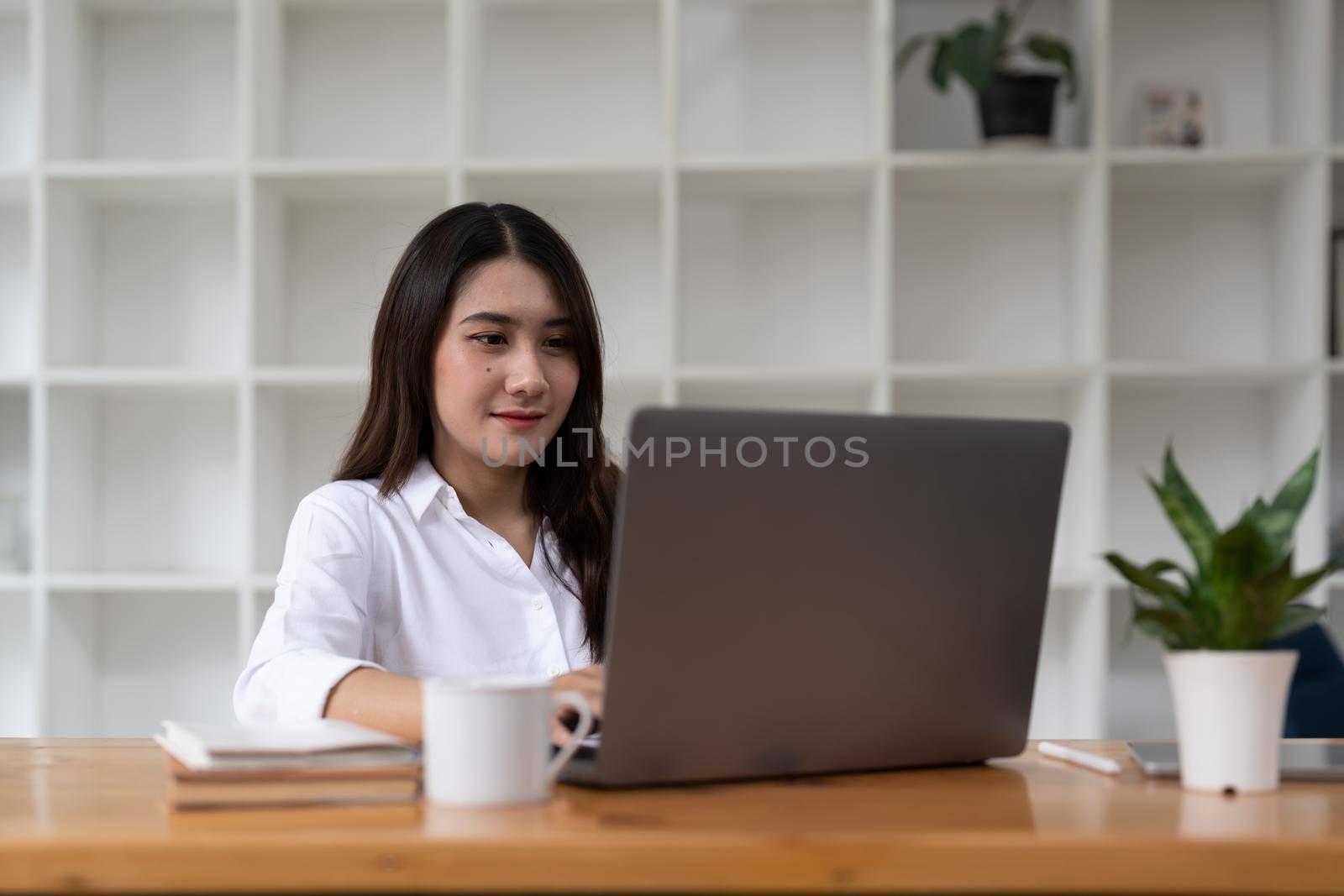 Young happy Asian businesswoman working from home and use a computer laptop and thinking idea for her business.