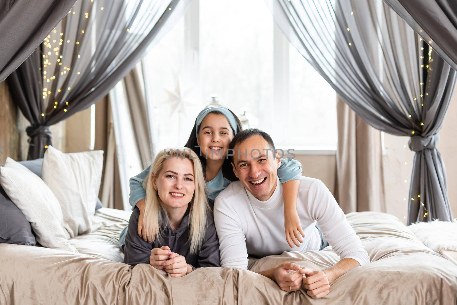 Smiling family lie on a white bed.