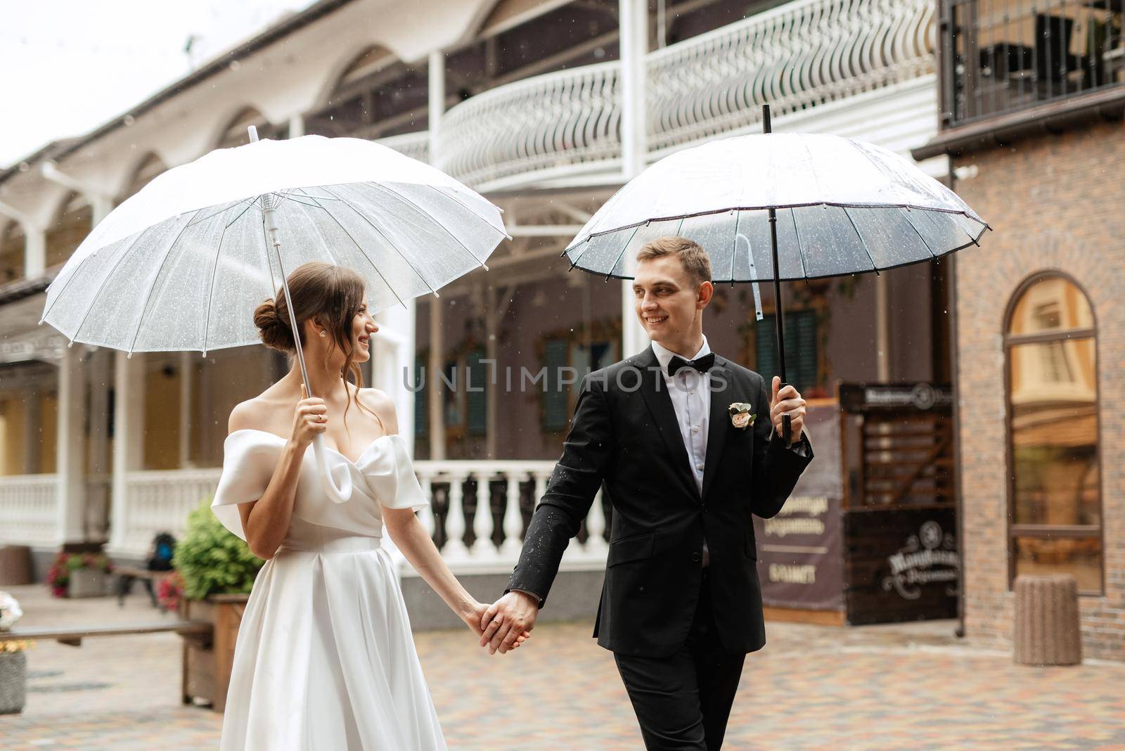 young couple bride and groom in a white short dress walking in the rain