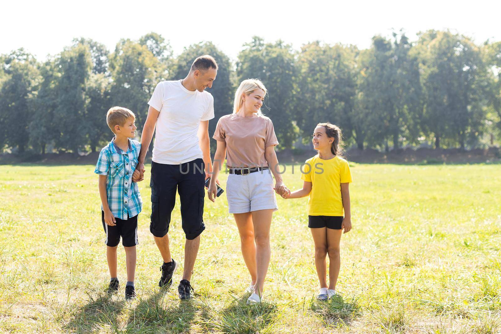 Happy loving family walking outdoor in the light of sunset. Father, mother, son and daughter. by Andelov13