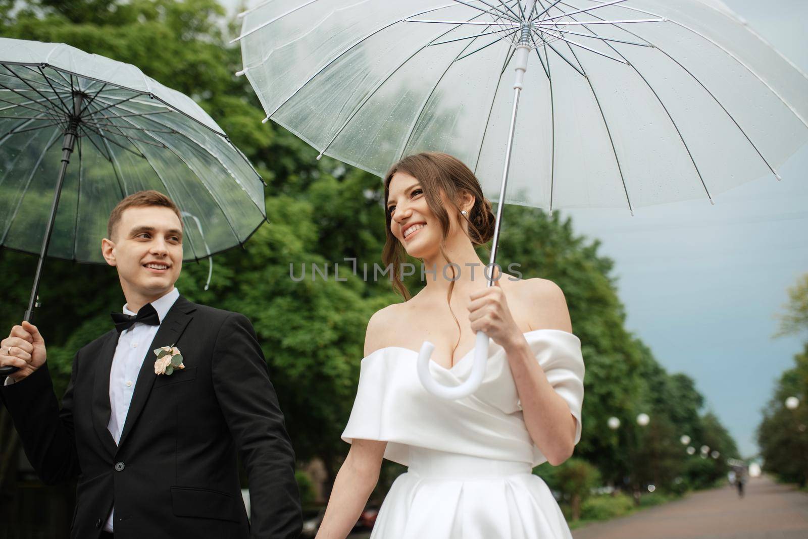 young couple bride and groom in a white short dress walking in the rain