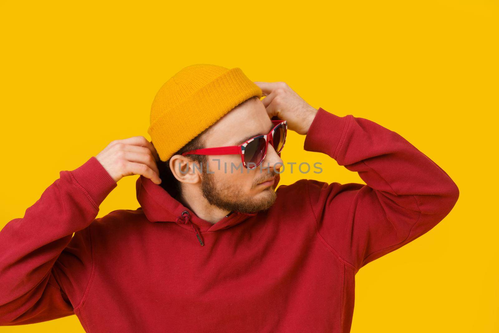 Close up portrait of pensive young man in casual wear in sunglasses posing sideways on yellow background. Stylish bearded smart hipster man casual look. Thoughtful guy on yellow background by LipikStockMedia