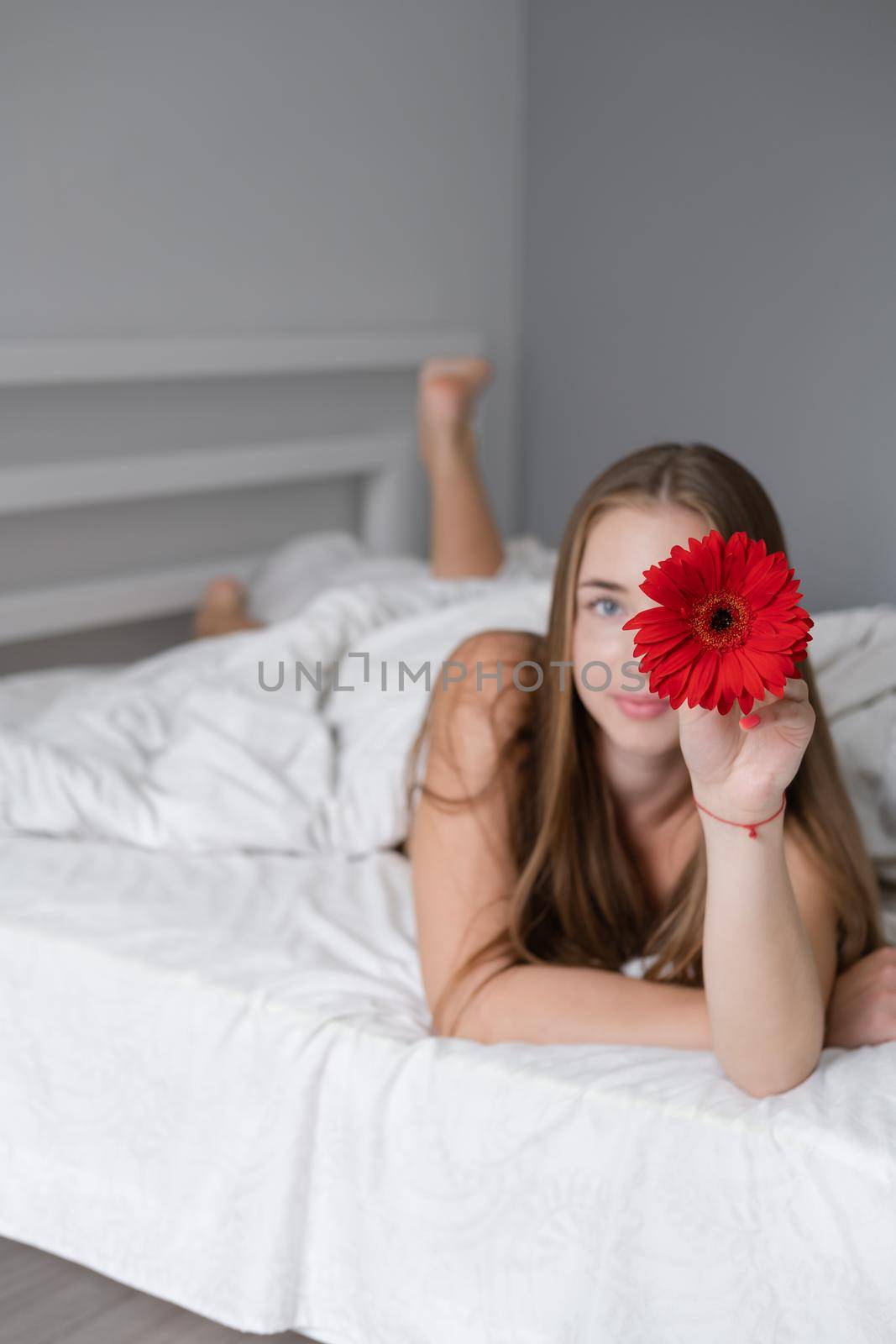 Calm woman with flower lying on her bed. morning routine. successful date. bright white bedroom.
