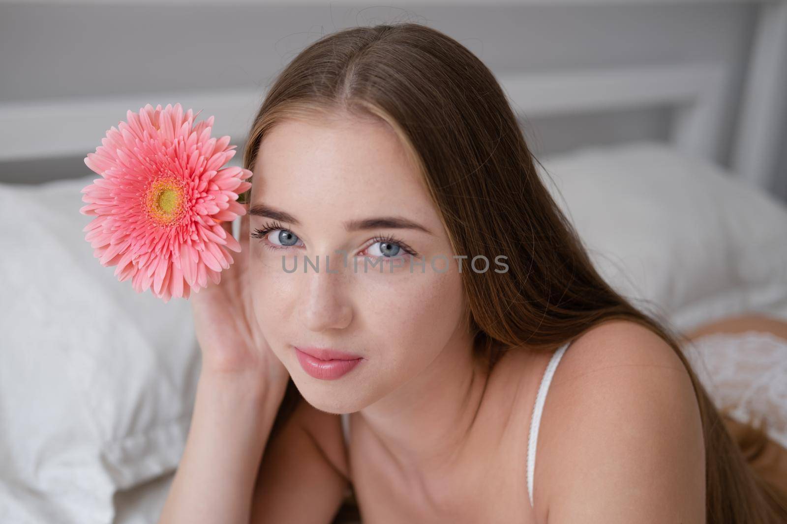 charming young woman lies in underwear on comfortable bed. holding red pink flower. tender portrait of a girl in a hotel room or home. Lovely female enjoy good relaxation. Morning time.