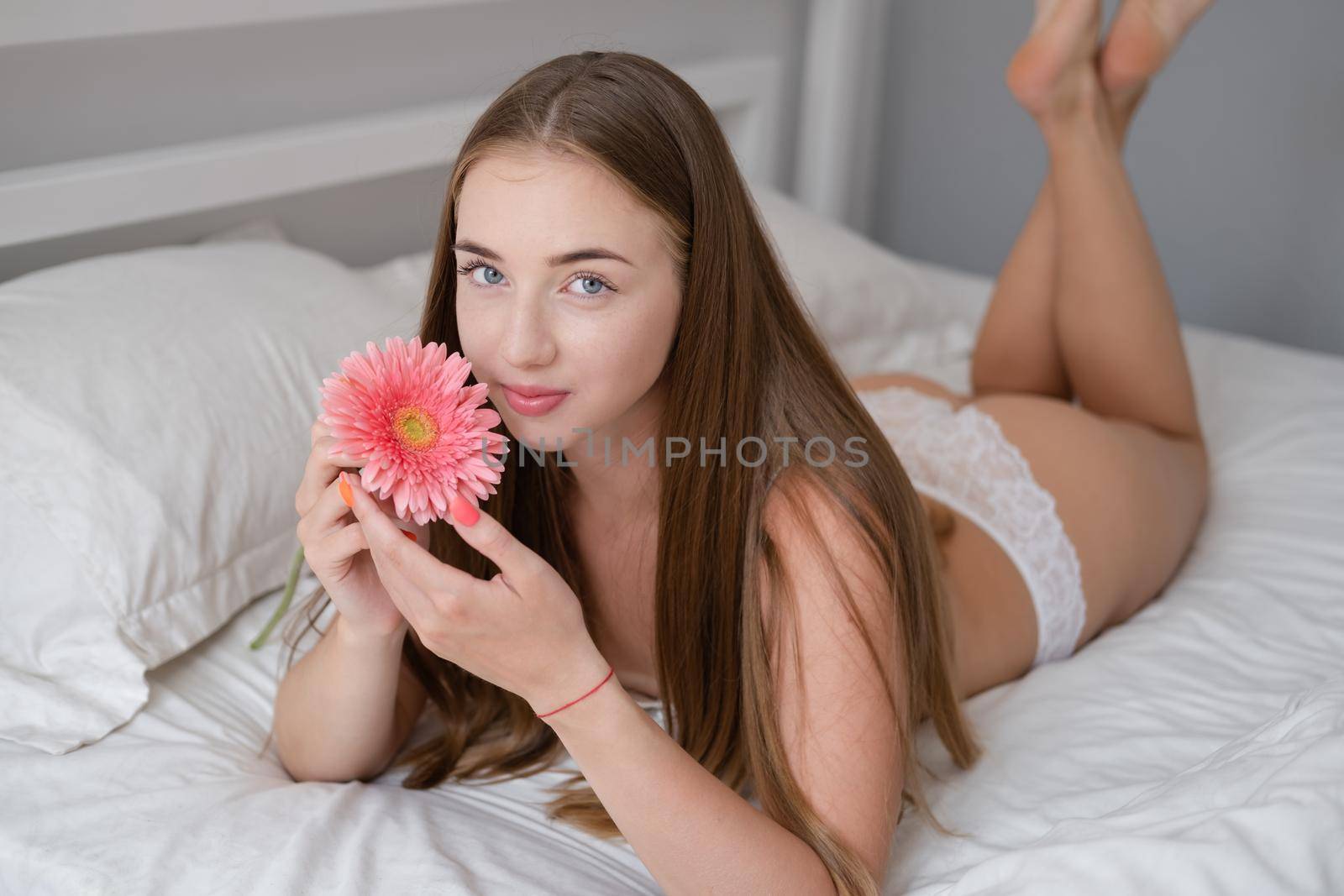 Calm woman with flower lying on her bed. morning routine. successful date. bright white bedroom.