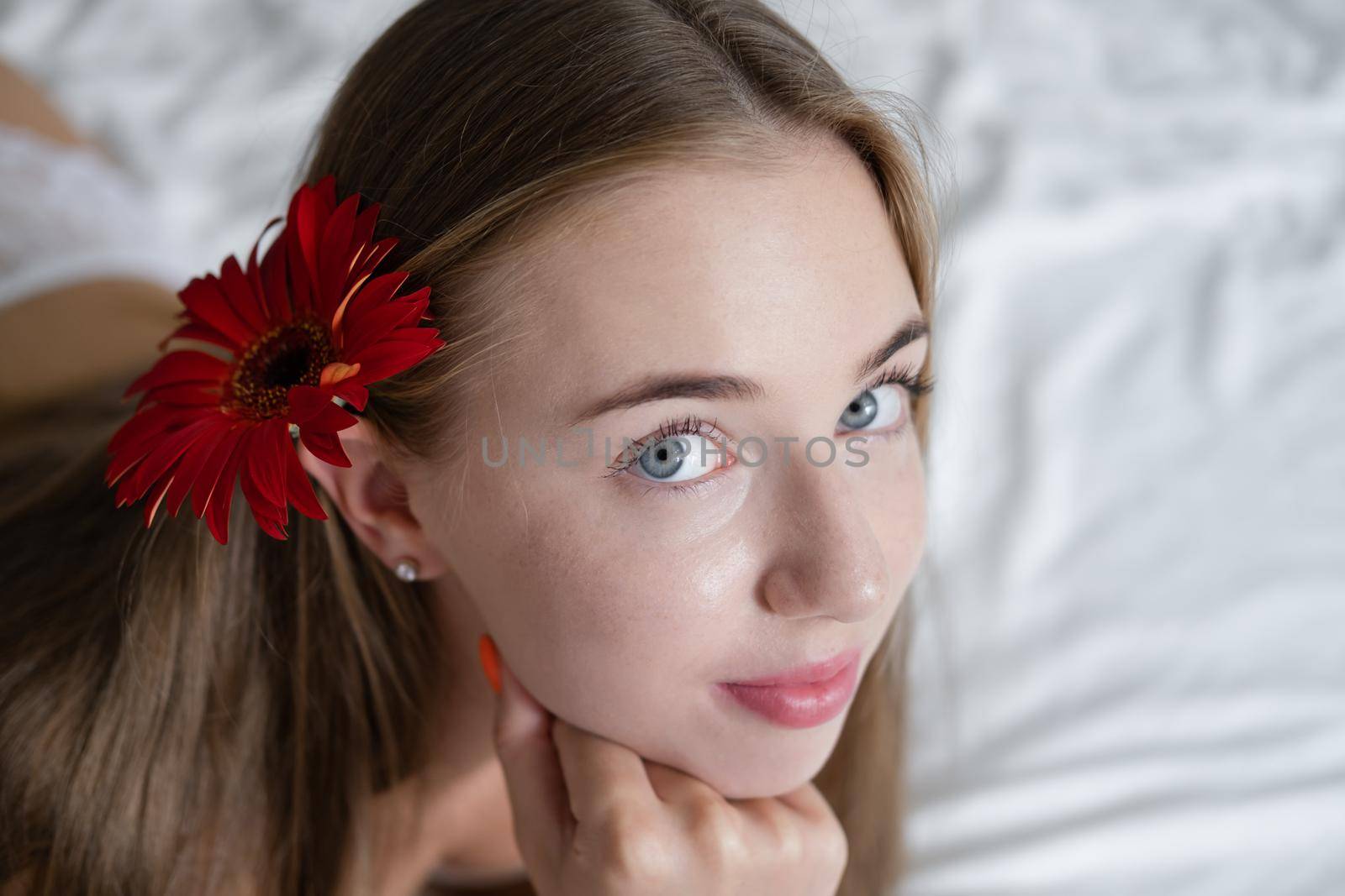 portrait of young woman in underwear on bed. holding red pink flower. female in a hotel room or home. white bedroom and bed sheets bedclothes. happy wonderful day by oliavesna