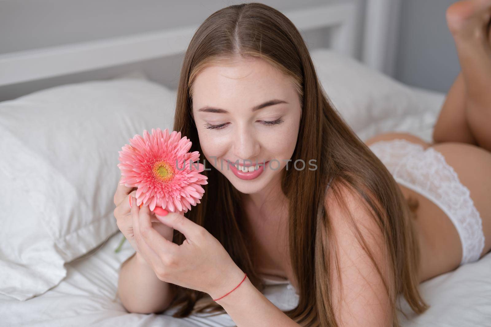 Calm woman with flower lying on her bed. morning routine. successful date. bright white bedroom.