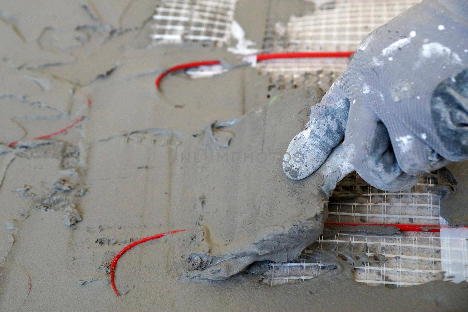 a worker applies cement mortar on an electric cable underfloor heating with a spatula close-up
