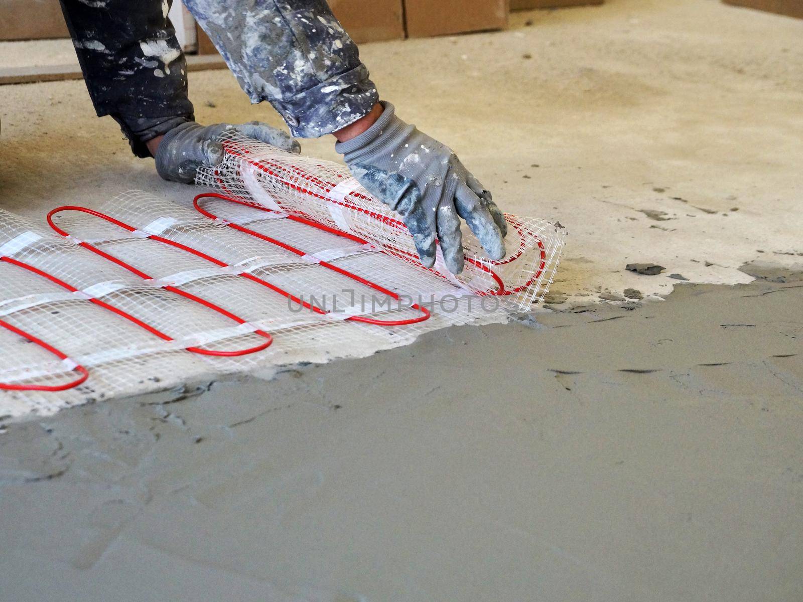 a worker unfolds a roll of warm electric floor for laying under a cement screed close-up