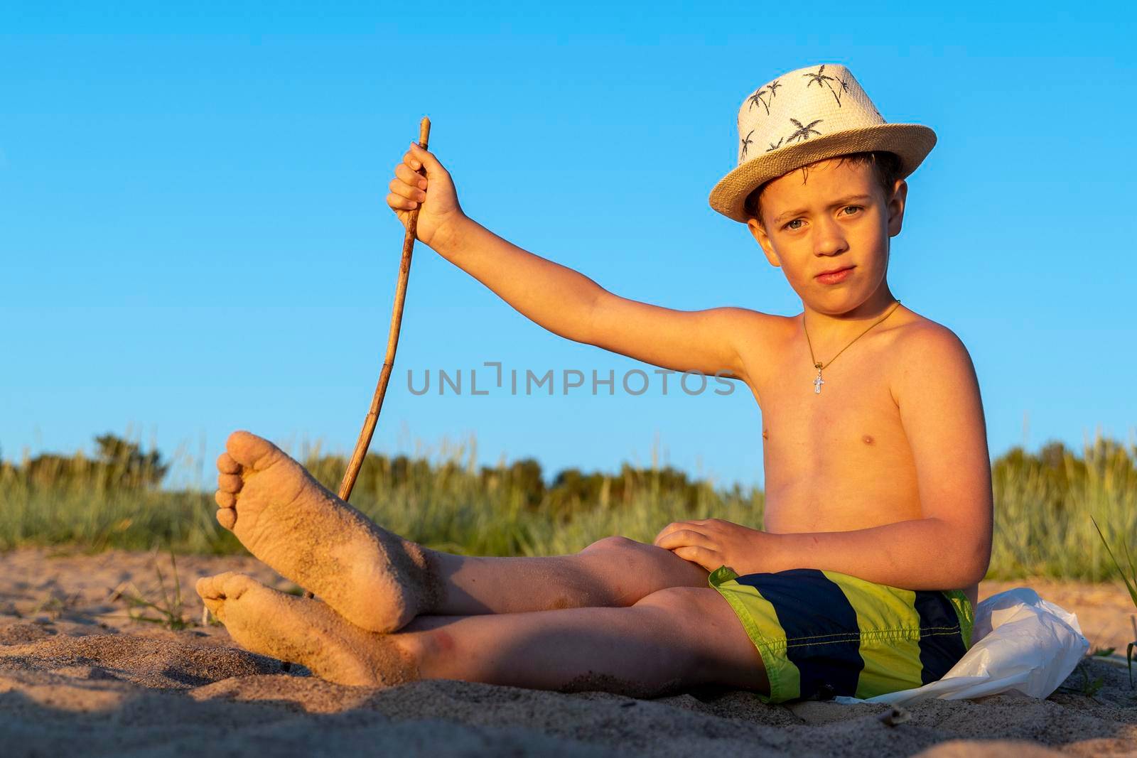 boy in a sun hat and swimming shorts is relaxing sitting on the beach by audiznam2609