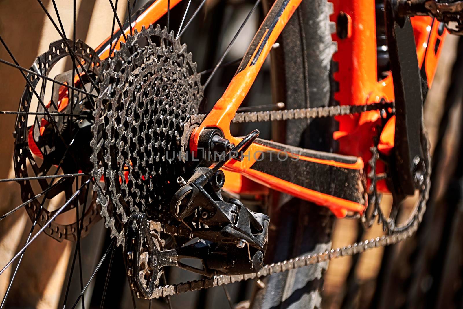 Bicycle rear wheel, wheel sprockets, and chain. Orange and black, out-of-focus background, pedal