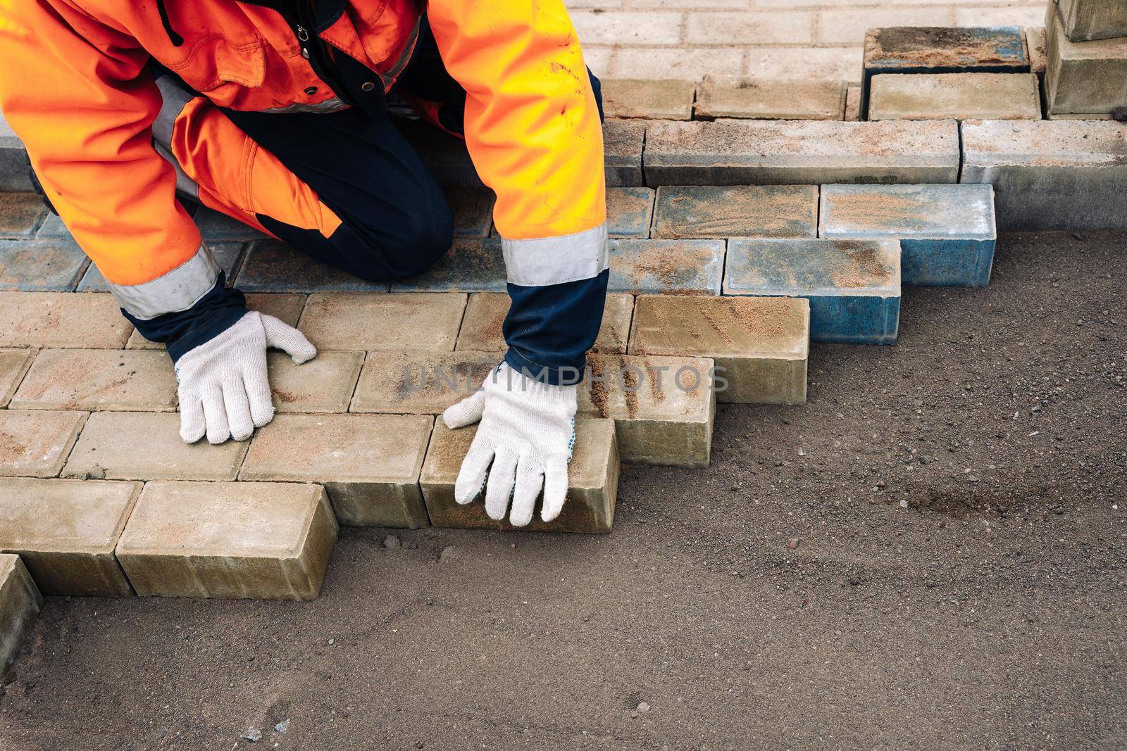 a worker in a protective work suit lays paving slabs. A professional master in work gloves lays paving stones. Paving of the site. Laying paving slabs in the yard of the house on a sandy foundation