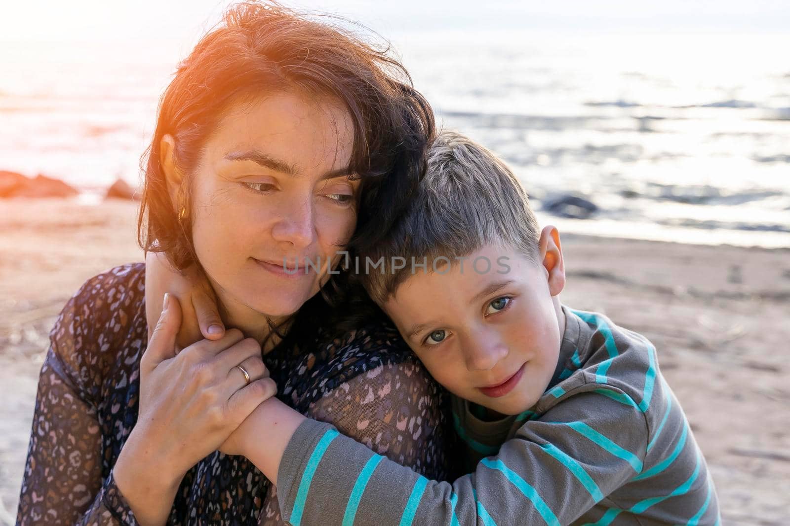 A cute happy preschooler boy hugs his mom on the seashore in the sunset rays. love for parents. Mother's Day