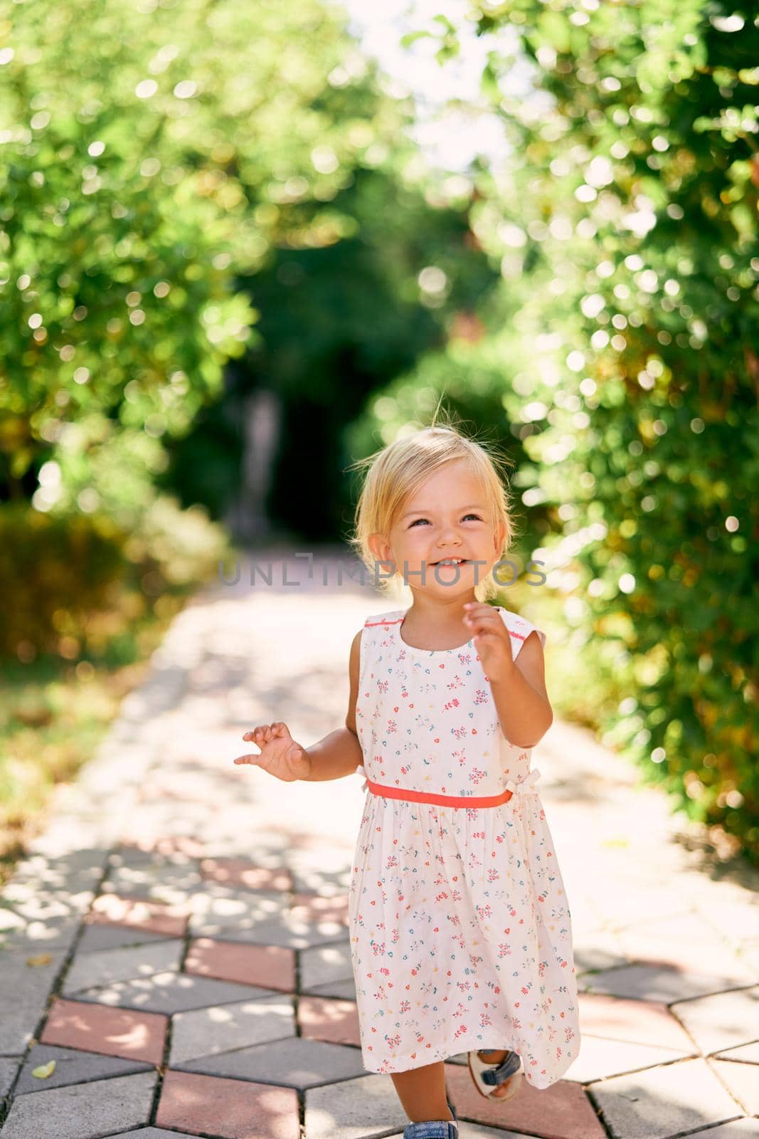 Little smiling girl runs along the paving stones in a green park. High quality photo