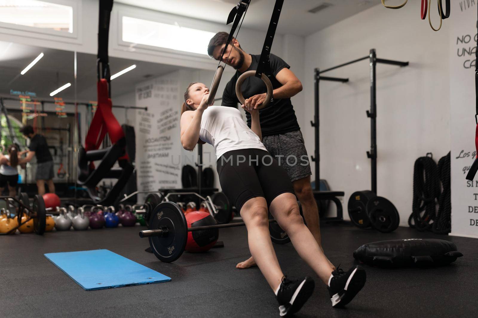 Young woman plays sports and performs single arm ring row and ring hold, at local training and fitness center, together with her personal trainer