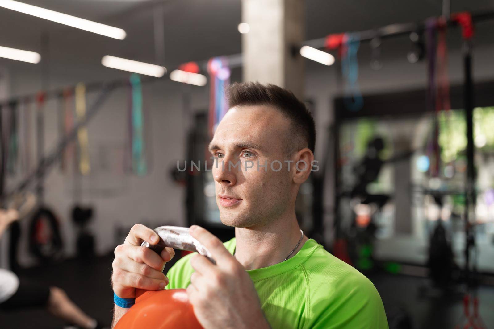 A young man holding the kettlebell with his hands, at the fitness center by stockrojoverdeyazul