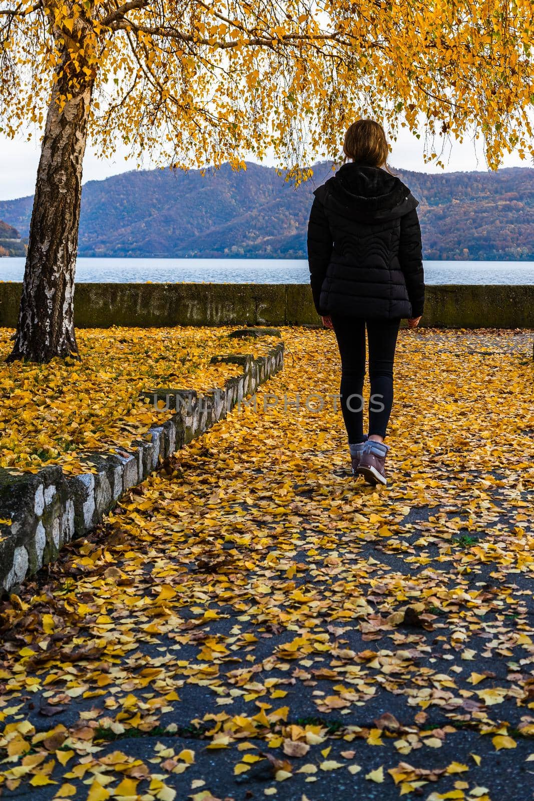 Autumn leaves fallen on alone woman walking on the autumn alley. Autumn landscape, orange foliage in a park in Orsova, Romania, 2020