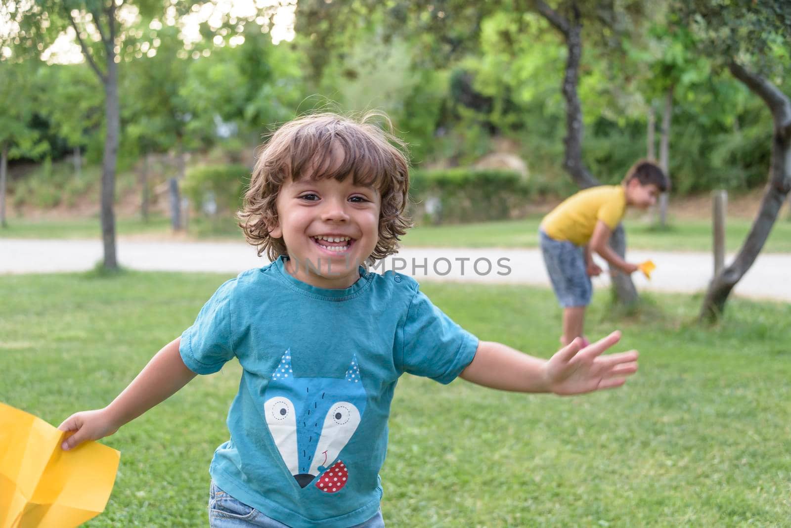 Boy playing toss paper plane outdoors looking away. Portrait of a cheerful caucasian boy playing in the spring and summer park having fun on the weekend