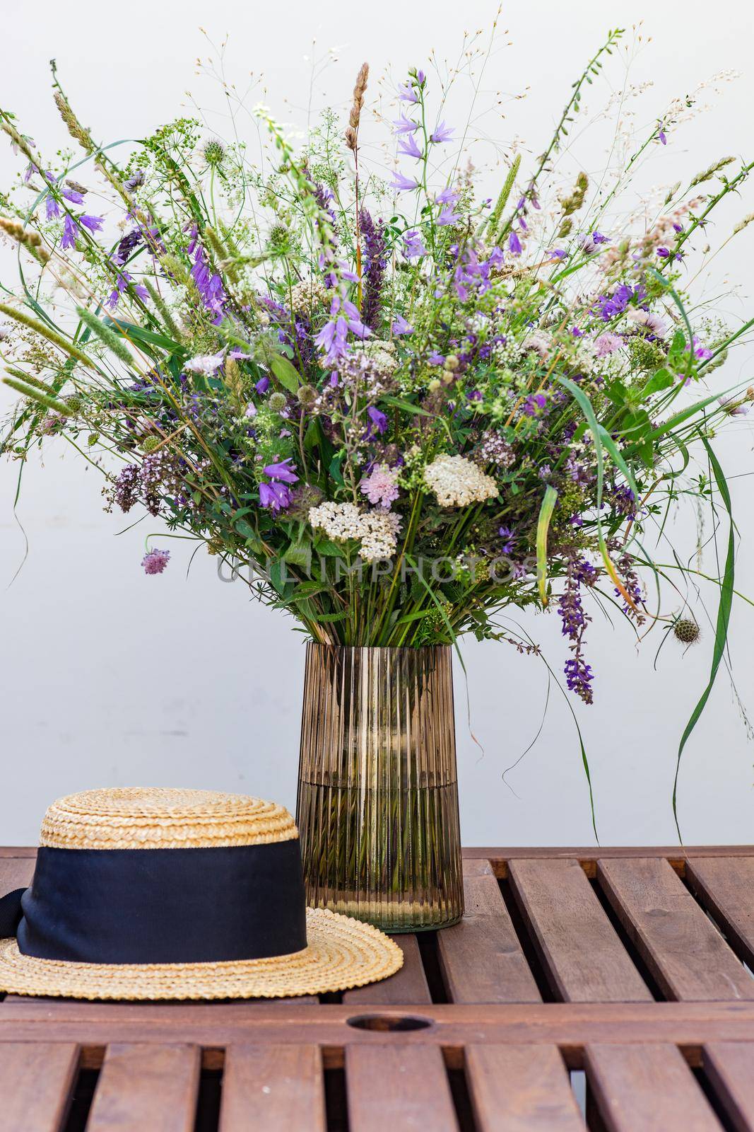 Beautiful wild flowers in bouquet and straw hat on wooden table