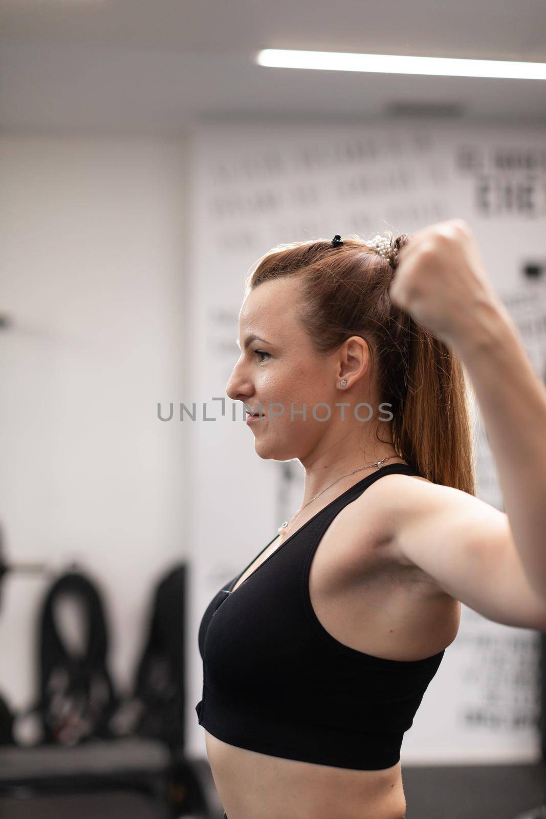 A young woman looks in front of a mirror, while making figures with her arms and muscles to observe how she is improving her physical shape at the local sport and fitness center