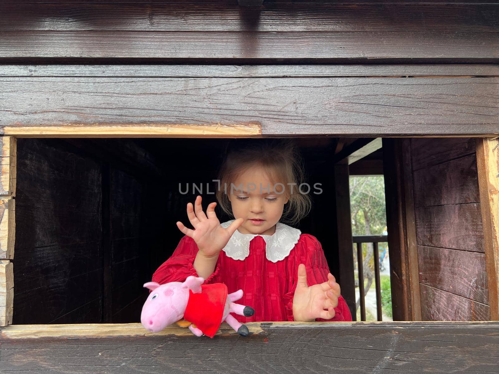 Little girl in a wooden gazebo by the window with a soft toy by Nadtochiy