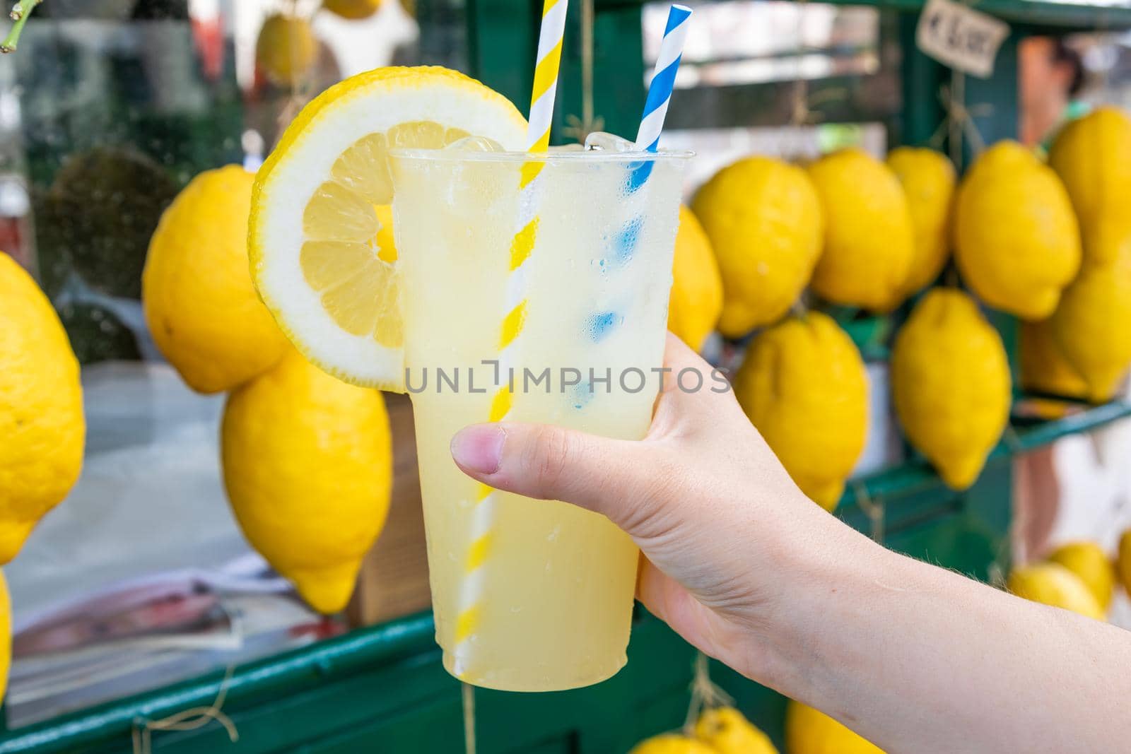 Caucasian hand with healthy fresh lemonade during summer with lemons background