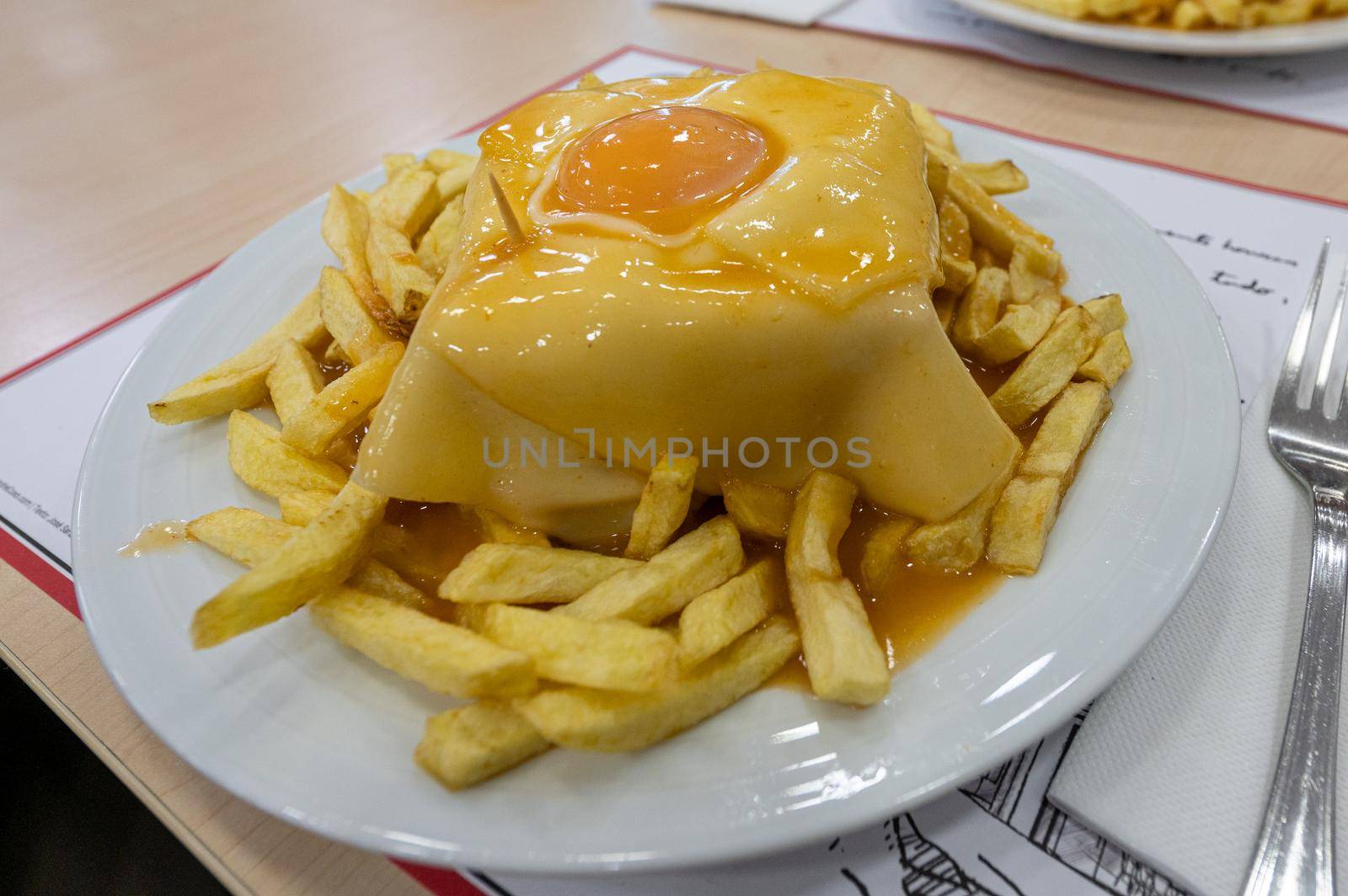 Traditional portuguese sandwich with sauce francesinha on dish.