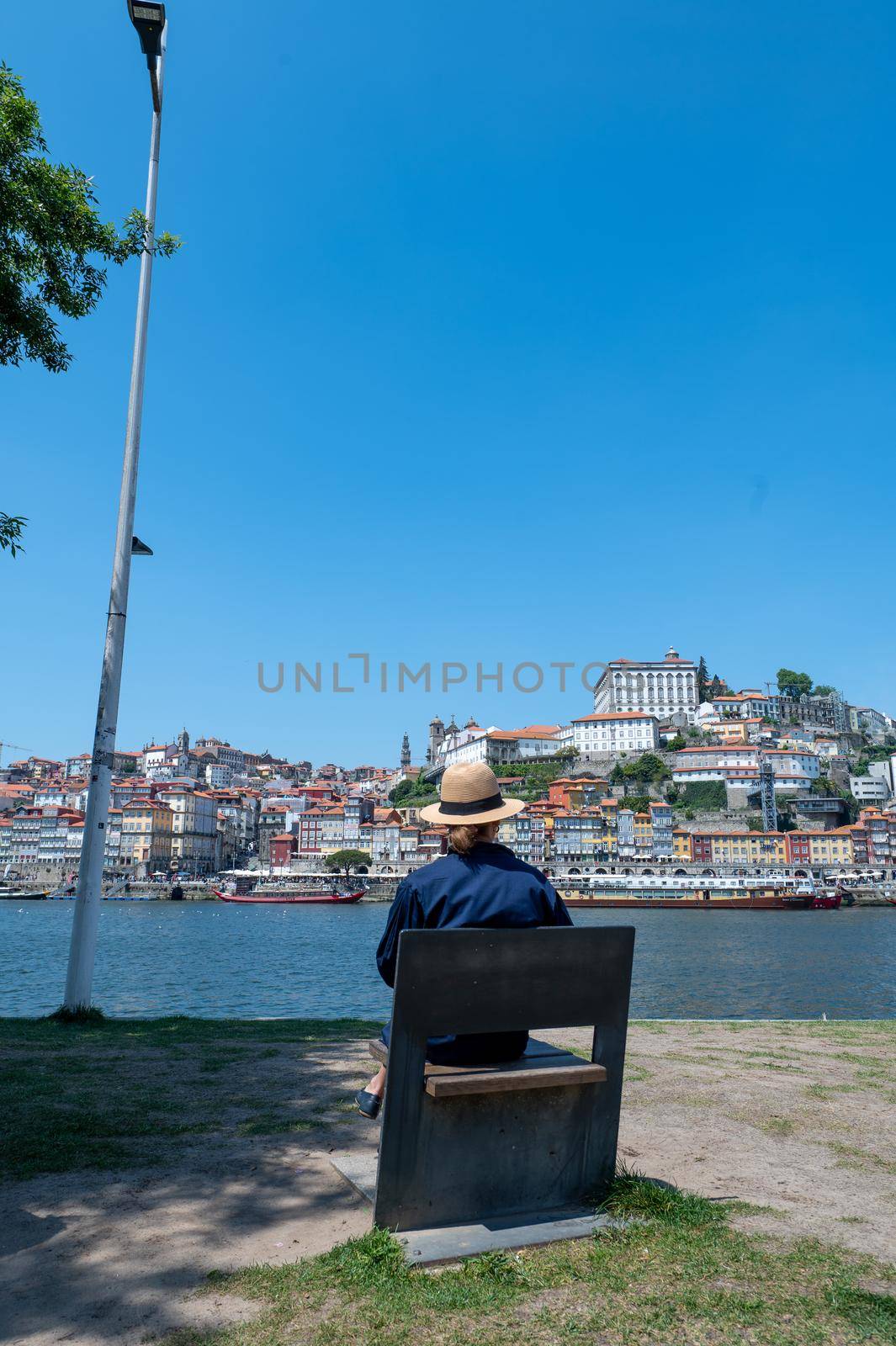 Woman with hat sitting on the shore of the Rio Douro in Porto, Portugal.