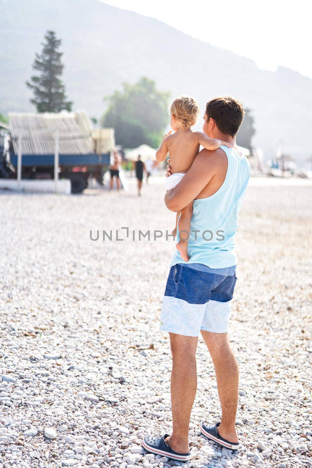 Dad with a little daughter in his arms stands on a pebble beach. High quality photo