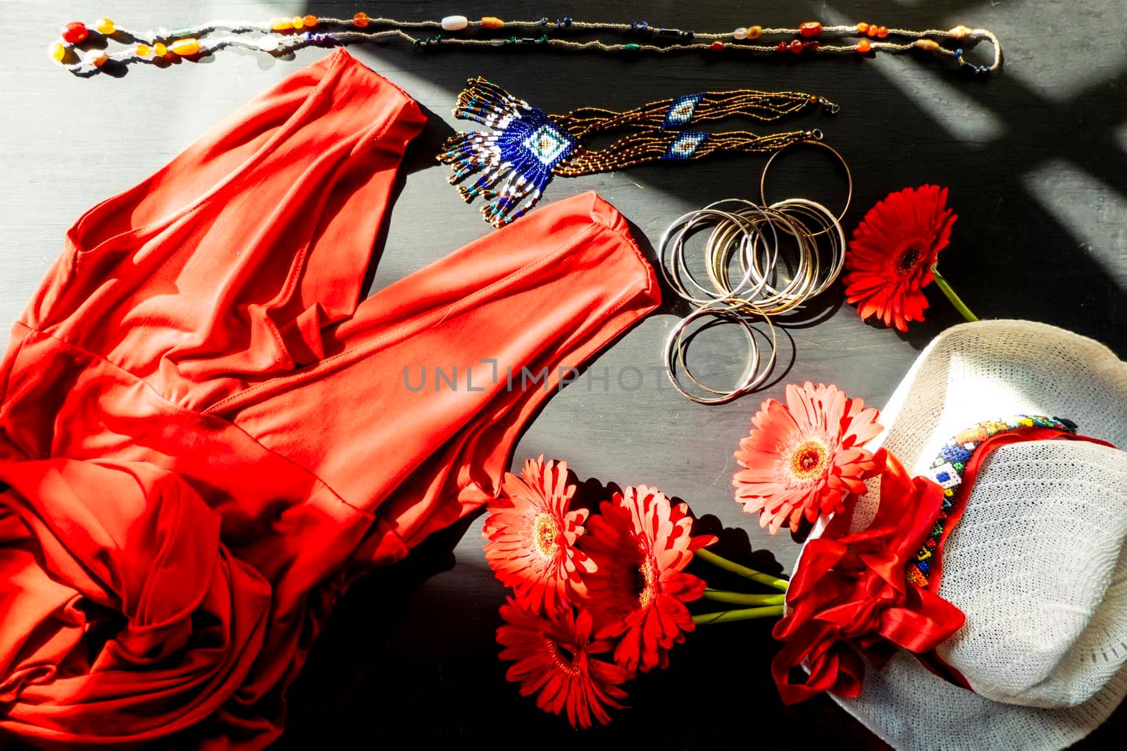 flat lay of a fashionable look from red and white accessories on a black background. Scarlet dress and white hat with a ribbon, jewelry made of beads and small stones, light jingling bracelets