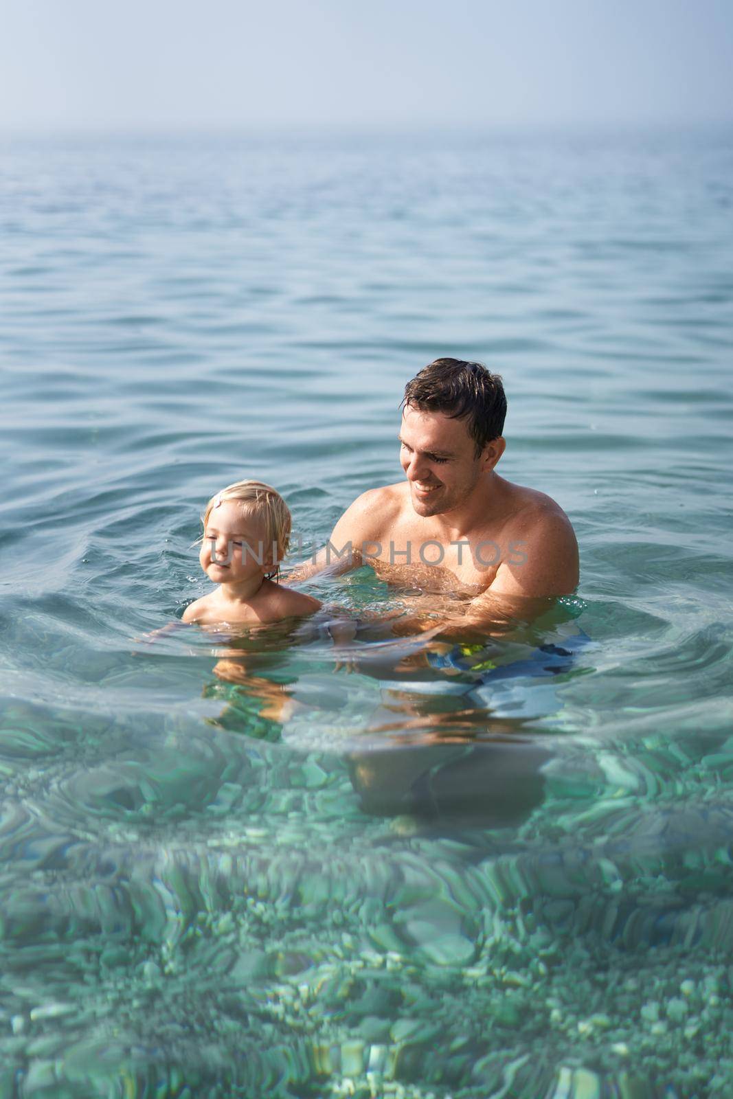 Smiling dad teaching little girl to swim by Nadtochiy