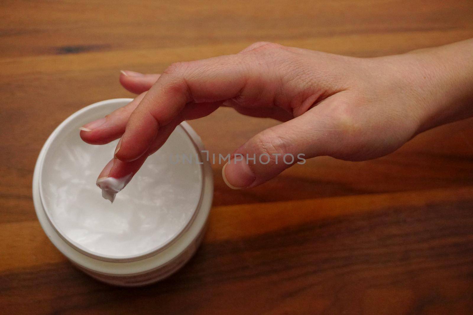 Woman applies hand cream to her hand on wooden isolated background