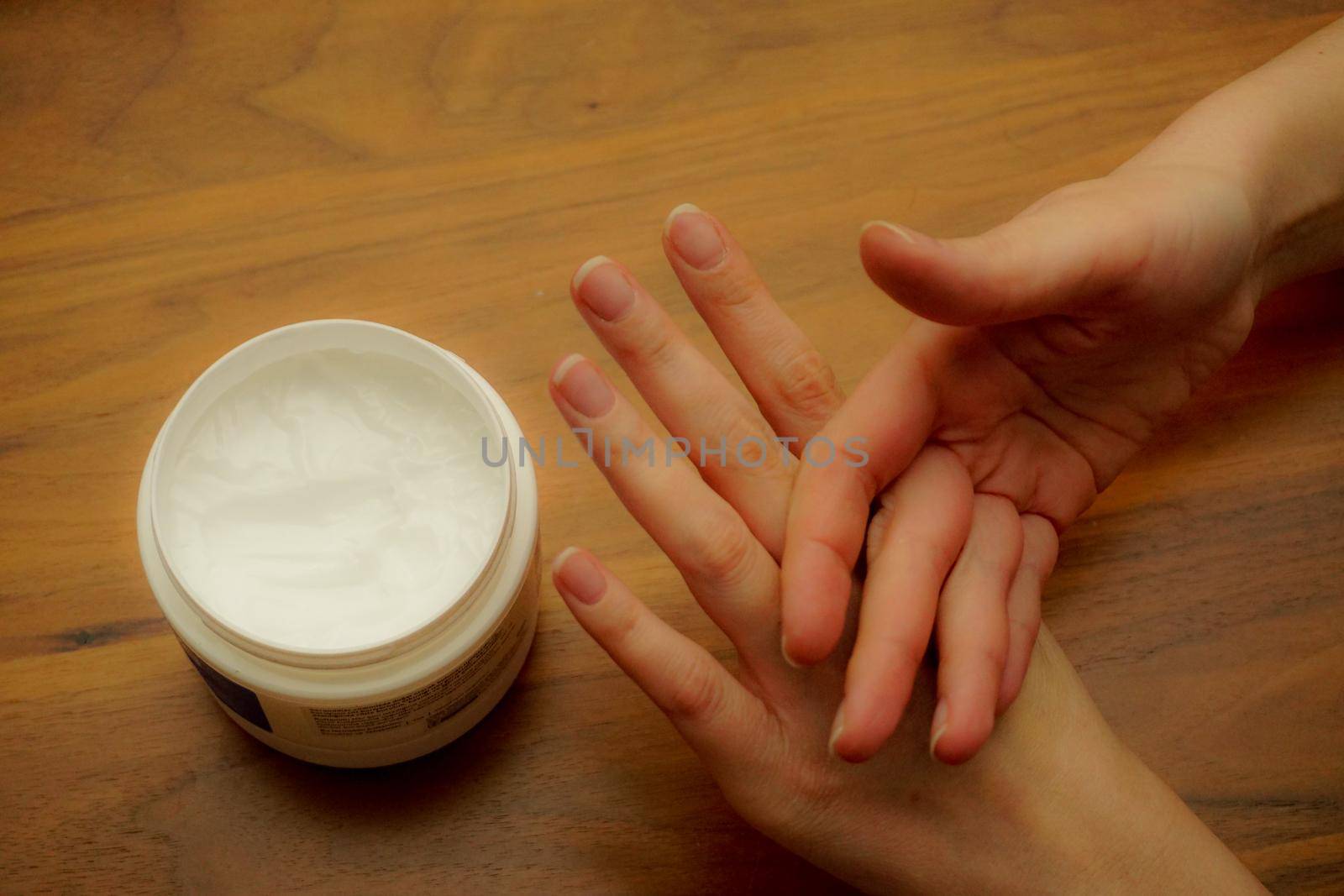 Woman applies hand cream to her hand on wooden isolated background by tasci