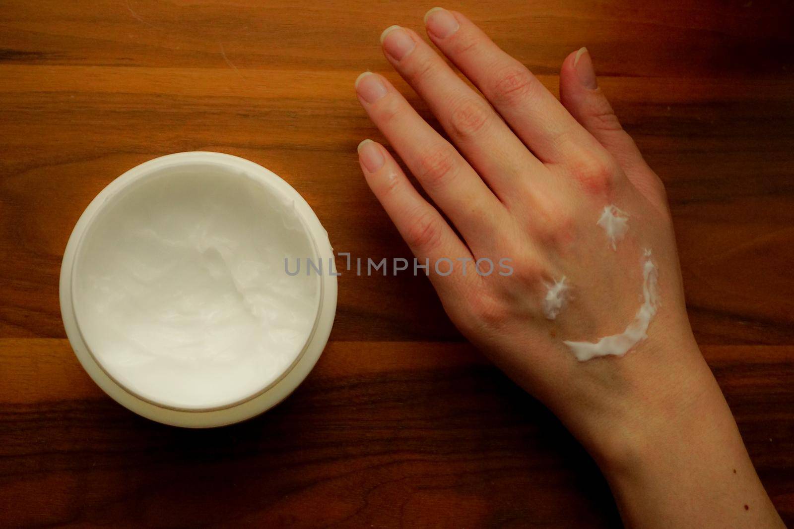 Woman applies hand cream to her hand on wooden isolated background