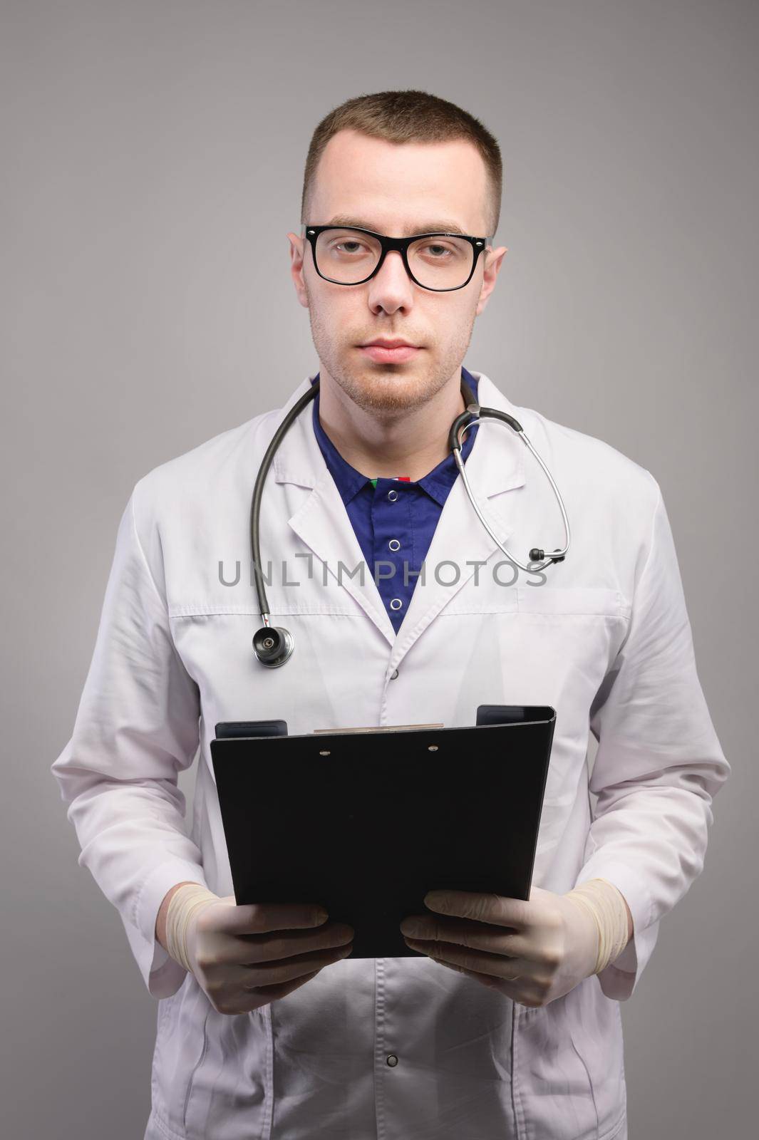 Portrait of a young medical specialist in a white coat, standing with a folder with tests in his hands. Studio shot.
