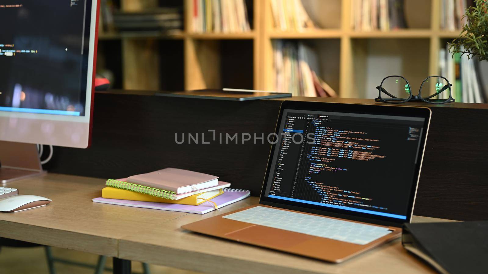 Laptop and computer pc on wooden office desk with programming code on screens.
