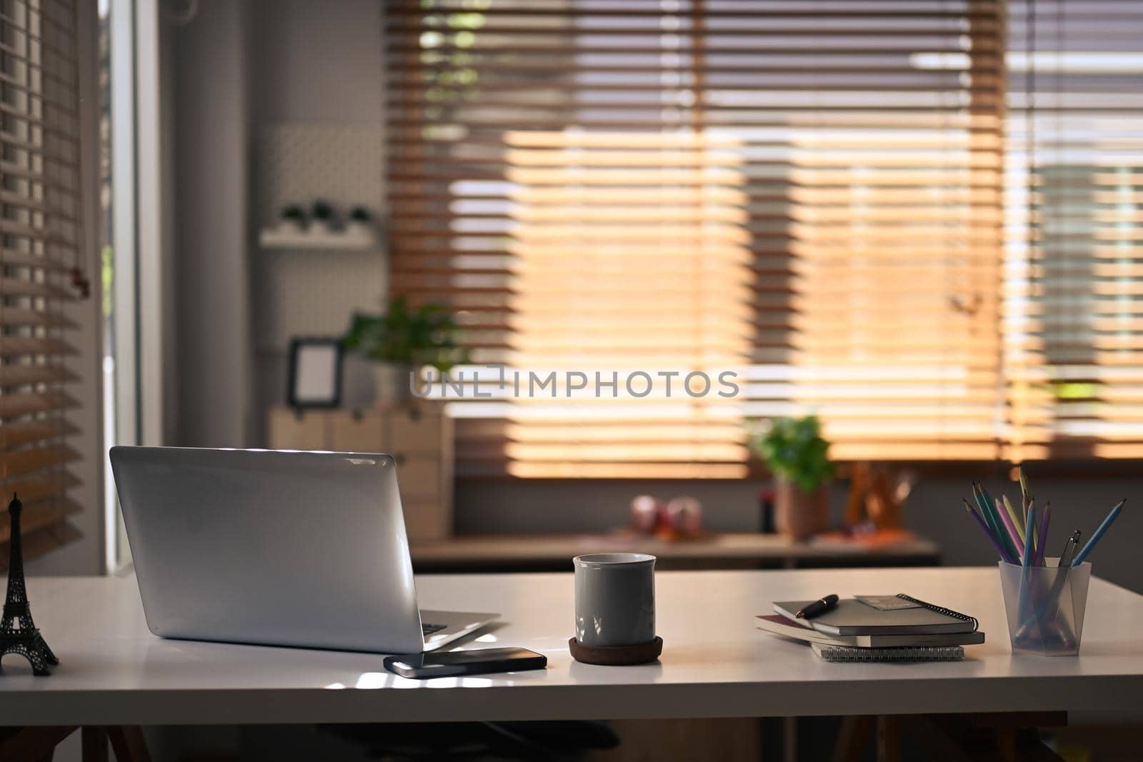 Contemporary home office. Computer laptop, coffee cup, notebooks and pencil holder on white table.