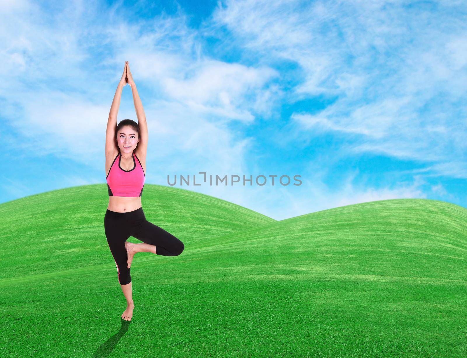 Young woman doing yoga exercise on grass with sky