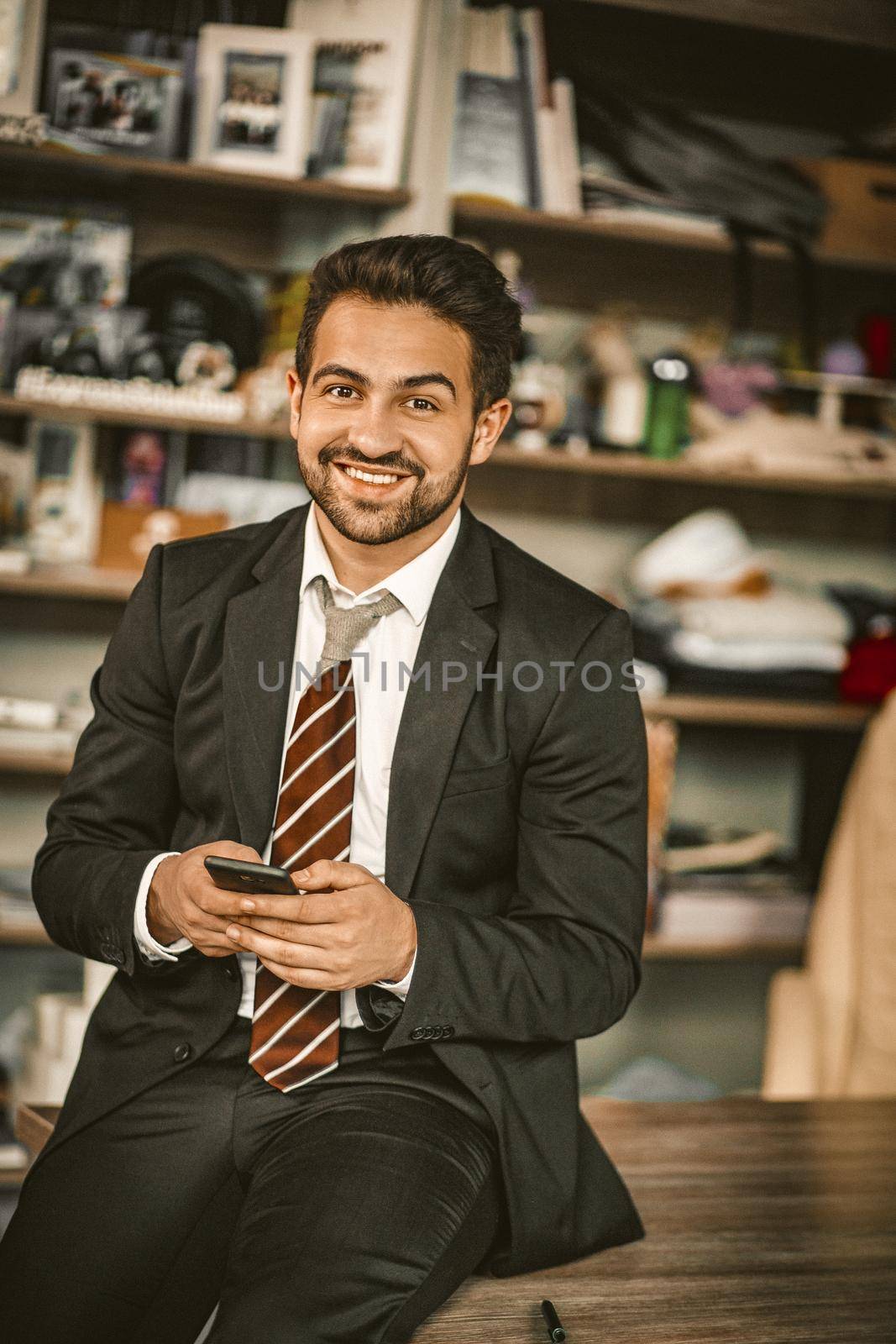 Well-dressed Business Man Relaxing During Office Break, Smiling Entrepreneur Looks At Camera Holding Mobile Phone While Sitting On Table, Handsome Man In Formalwear Chatting By Phone, Toned Image