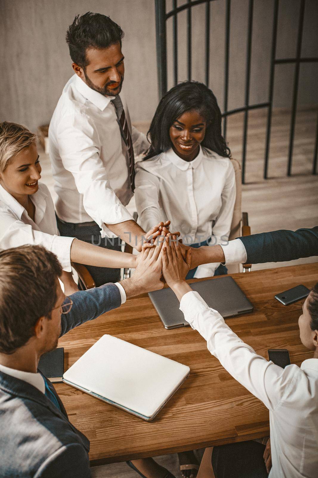Smiling Business People Joined Their Hands In High Five As Gesture Of Unity, Diverse Team Of Male And Female Coworker Give High Five Sitting Together At Table In Boardroom, Toned Image