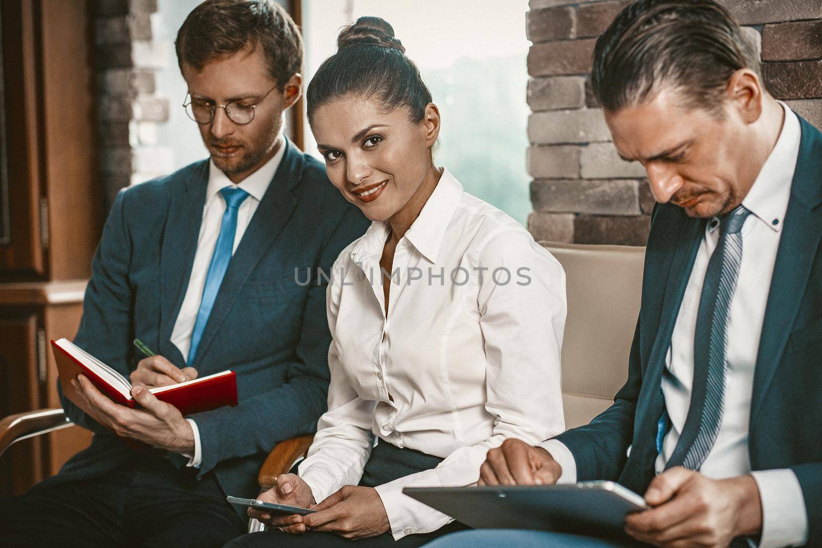 Business Colleagues Are Preparing To Hand Over The Meeting Reports, Men Making Notes And Using Laptop While Sitting On Sofa, Focus On Smiling Lady Typing On Phone And Looking At Camera, Toned Image