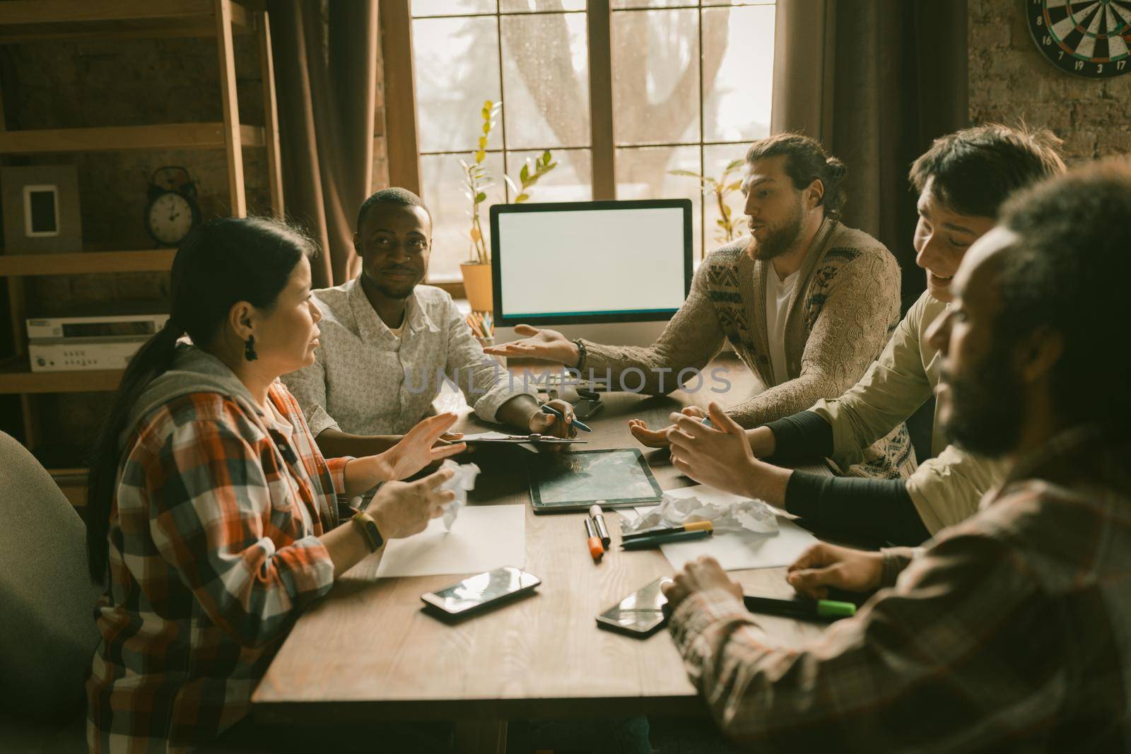 Diverse Freelancers Team Planning Startup Project, Creative People Talks Gesticulating With Hands While Sitting At Office Desk With Monitor On It, Focus On African Man's Hands Holding Pen And Paper