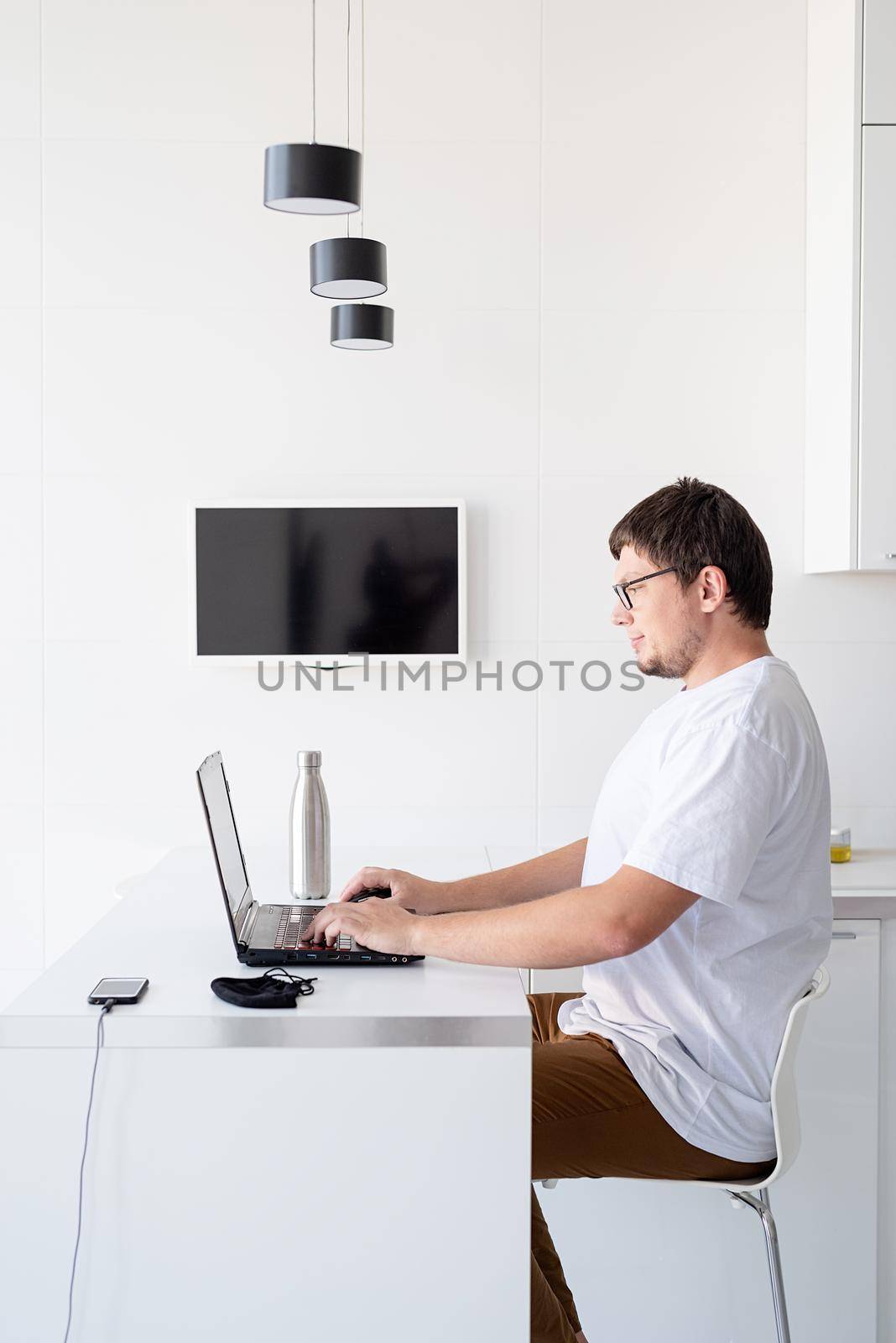 Social distancing. E-learning and teaching. Young smiling man in white shirt using laptop working from home