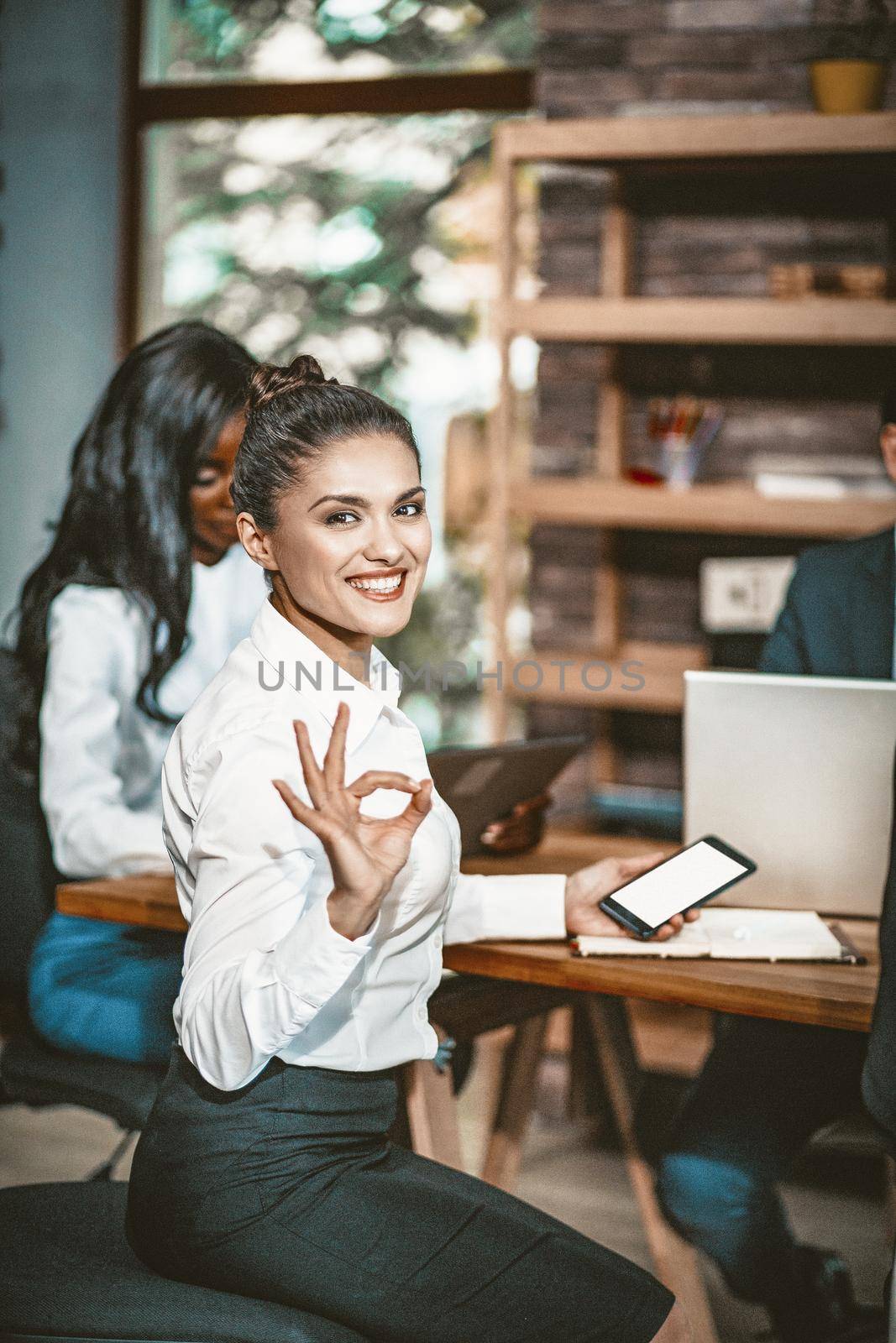 Smiling Businesswoman Showing Ok Sign, Intelligent Woman Shows Okey Gesture Meaning That Everything Will Be Good With One Hand And Holding Phone In Other Hand, Toned Image